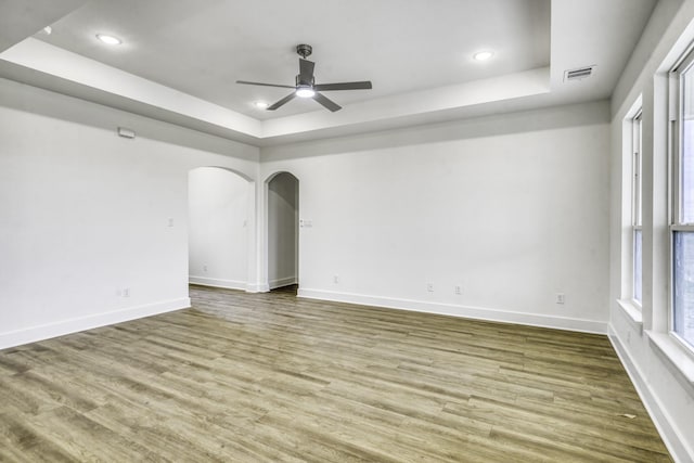spare room featuring a ceiling fan, a tray ceiling, wood finished floors, and arched walkways