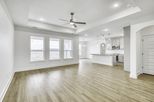 unfurnished living room with a ceiling fan, visible vents, light wood-style flooring, a sink, and a raised ceiling