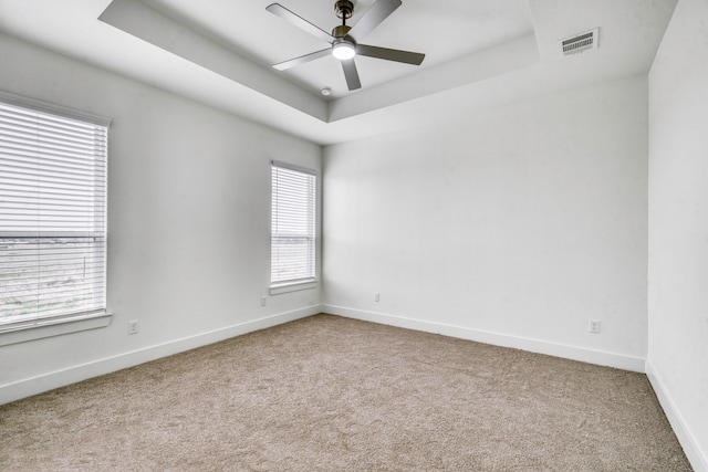 unfurnished room featuring visible vents, a ceiling fan, a tray ceiling, carpet floors, and baseboards