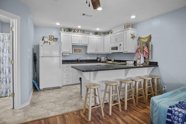 979 Sea Spray Dr, Crystal Beach, TX 77650 - kitchen with white appliances, visible vents, a breakfast bar, a peninsula, and white cabinetry