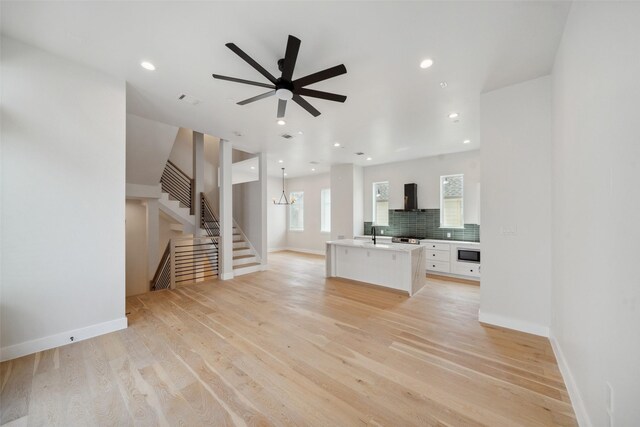 unfurnished living room with stairs, baseboards, ceiling fan, and light wood-style flooring