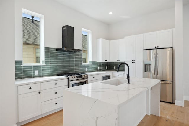 kitchen with light stone countertops, a sink, wall chimney exhaust hood, stainless steel appliances, and white cabinetry