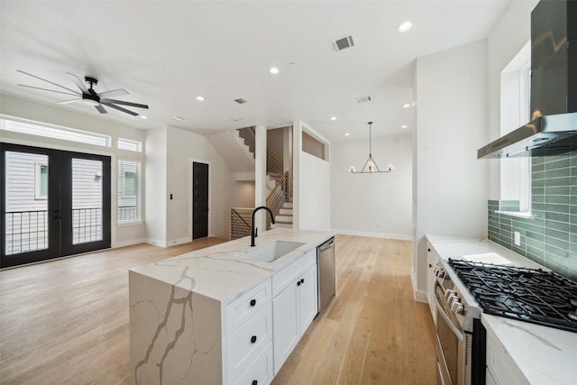 kitchen with visible vents, open floor plan, wall chimney range hood, a sink, and appliances with stainless steel finishes