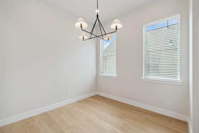 unfurnished dining area featuring baseboards, light wood-type flooring, and a chandelier