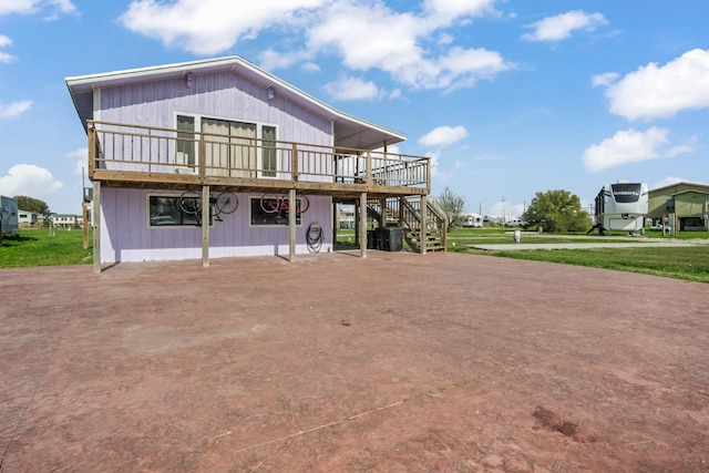 rear view of house with stairs, concrete driveway, and a wooden deck