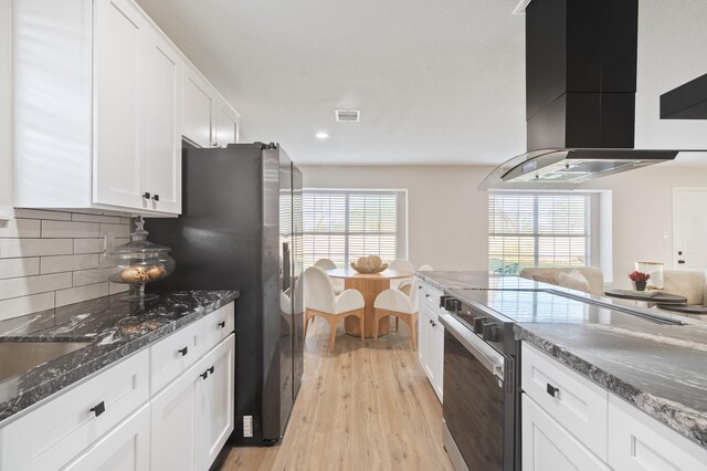 kitchen featuring visible vents, tasteful backsplash, stainless steel appliances, white cabinets, and wall chimney range hood
