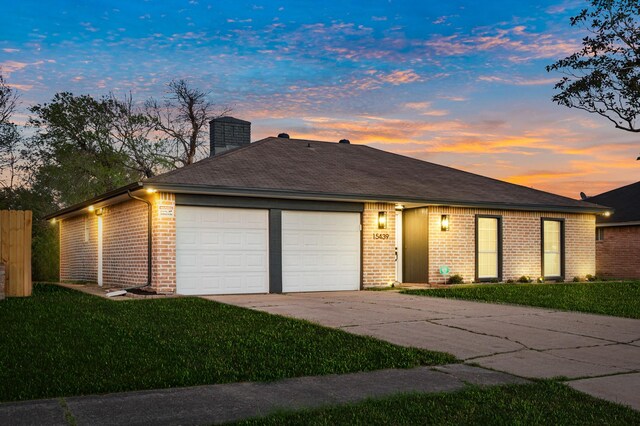 ranch-style house featuring brick siding, a lawn, a chimney, a garage, and driveway