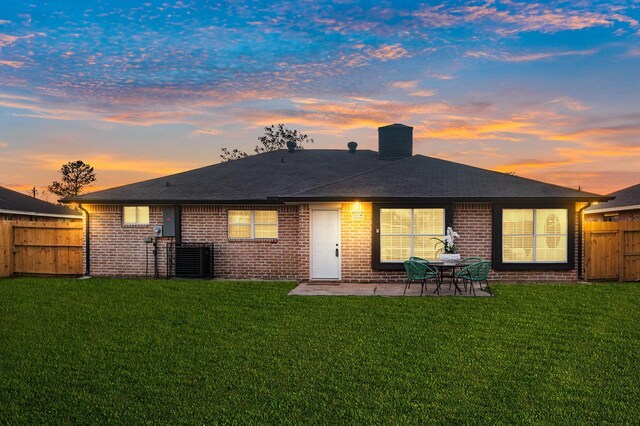 back of house at dusk with a patio, a lawn, a fenced backyard, and a chimney