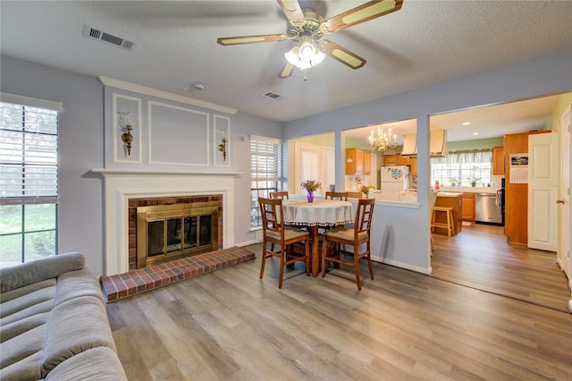 dining space featuring visible vents, ceiling fan with notable chandelier, a fireplace, and light wood finished floors