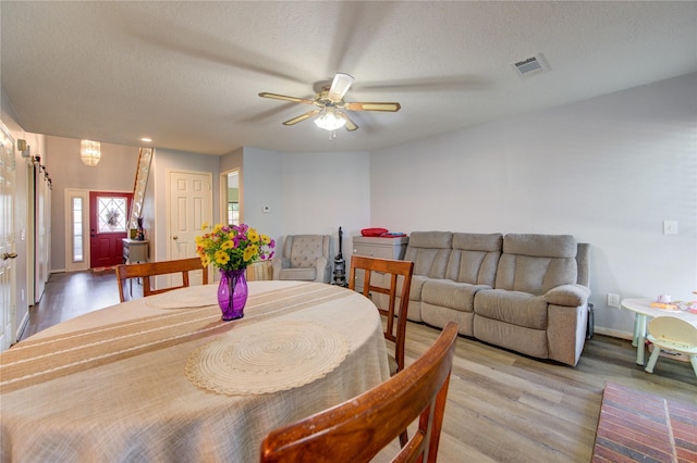 dining space with a ceiling fan, visible vents, wood finished floors, and a textured ceiling
