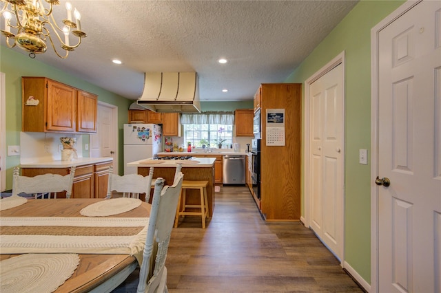 kitchen featuring an inviting chandelier, dark wood-type flooring, a kitchen island, wall chimney range hood, and appliances with stainless steel finishes