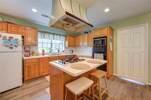 kitchen featuring light wood-type flooring, a kitchen bar, white appliances, and light countertops