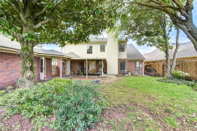 rear view of property featuring a patio area, a shingled roof, a lawn, fence, and brick siding