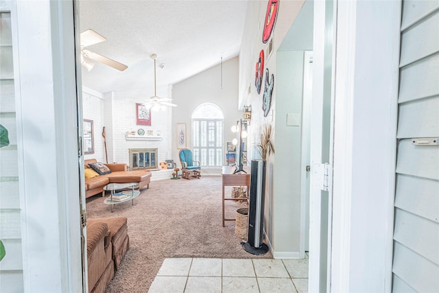 living area featuring light tile patterned floors, a ceiling fan, a textured ceiling, a brick fireplace, and light colored carpet