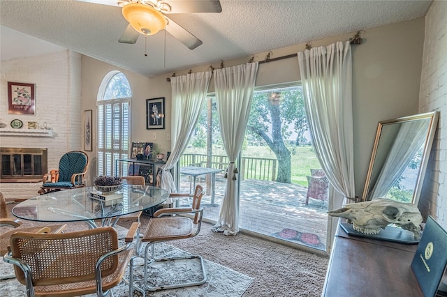 carpeted dining space with a textured ceiling, a fireplace, a ceiling fan, and vaulted ceiling