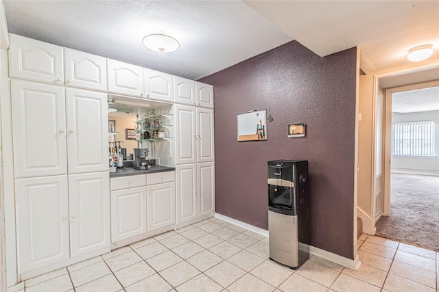 kitchen with white cabinets, light tile patterned flooring, baseboards, and light carpet
