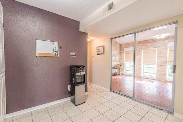 empty room with visible vents, brick wall, light tile patterned floors, baseboards, and a textured wall