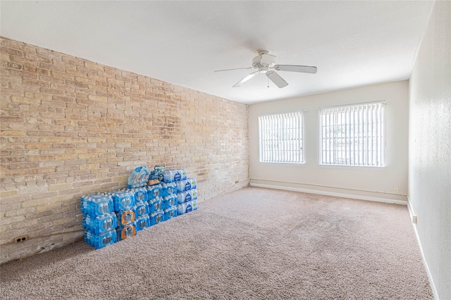 empty room featuring a ceiling fan, baseboards, brick wall, and carpet floors