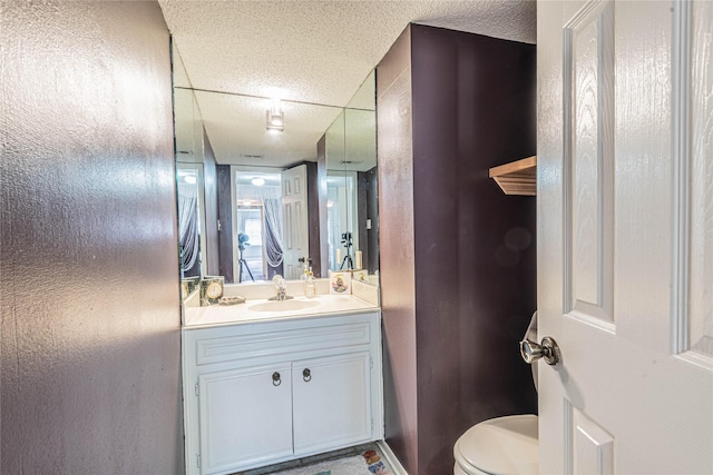 half bathroom featuring vanity, toilet, and a textured ceiling