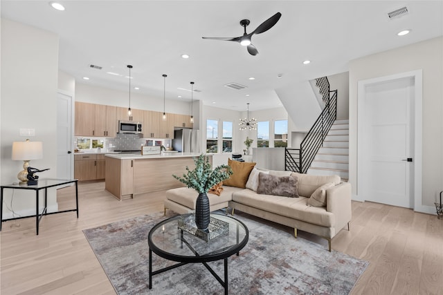 living area with stairs, light wood-style floors, ceiling fan with notable chandelier, and visible vents