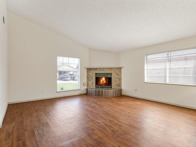 unfurnished living room with a textured ceiling, lofted ceiling, a lit fireplace, and wood finished floors