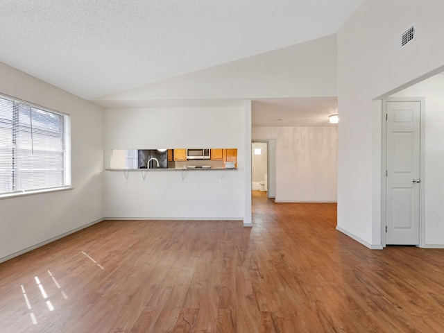 unfurnished living room with visible vents, baseboards, lofted ceiling, light wood-style floors, and a textured ceiling