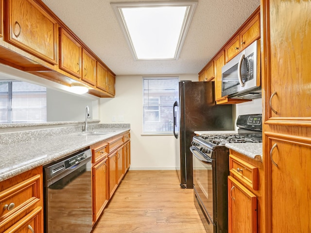 kitchen featuring light wood-type flooring, light countertops, brown cabinetry, black appliances, and a sink