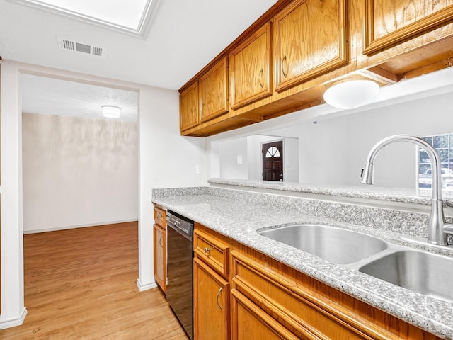 kitchen with visible vents, light wood finished floors, a sink, black dishwasher, and brown cabinets