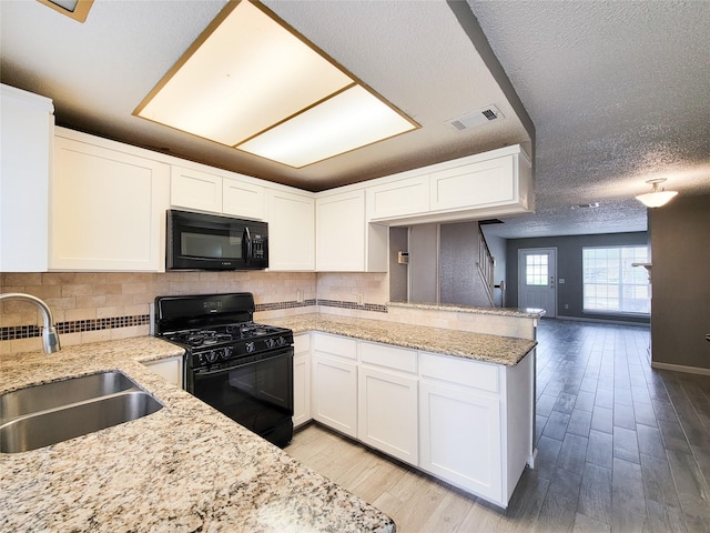 kitchen with visible vents, a peninsula, light wood finished floors, a sink, and black appliances