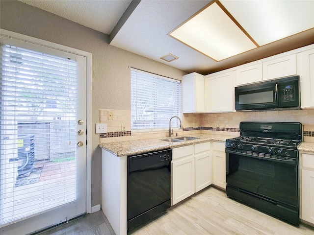 kitchen with a sink, black appliances, light wood-style floors, a textured wall, and backsplash