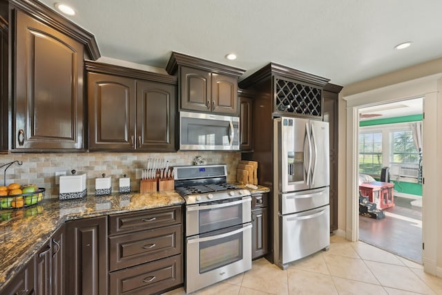 kitchen with light tile patterned floors, dark stone counters, stainless steel appliances, decorative backsplash, and dark brown cabinets