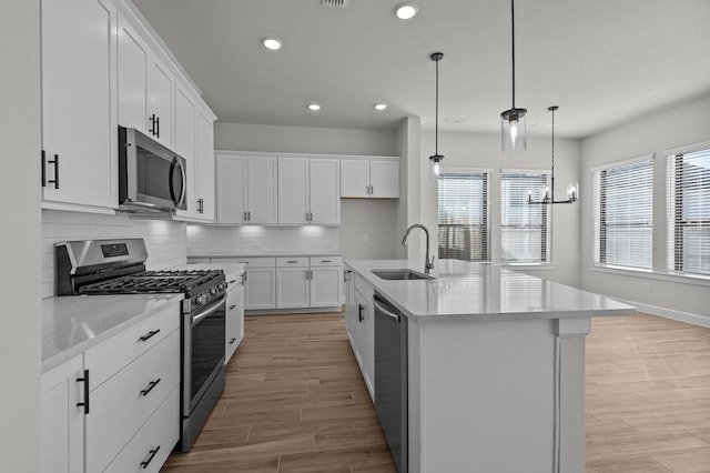 kitchen with light wood finished floors, backsplash, appliances with stainless steel finishes, white cabinets, and a sink