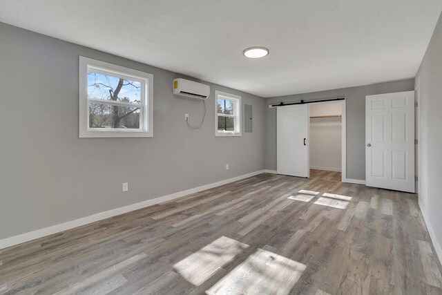 71 Deer Run Cir, Coldspring, TX 77331 - unfurnished bedroom featuring a wall mounted AC, a barn door, baseboards, wood finished floors, and electric panel