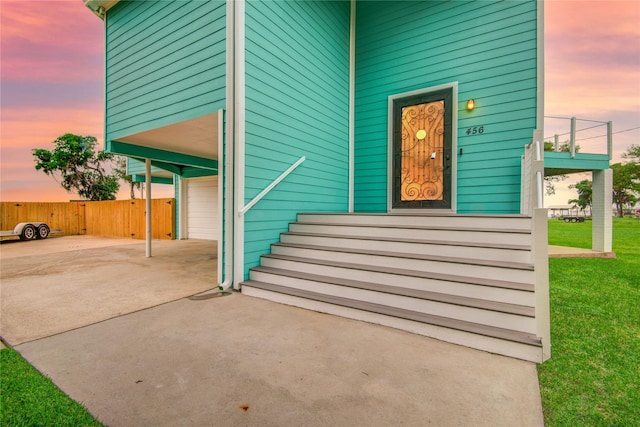 456 S Burnett Dr, Baytown, TX 77520 - exterior entry at dusk with fence, a yard, an attached garage, and concrete driveway