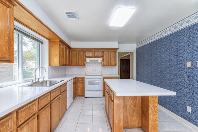 kitchen featuring visible vents, wallpapered walls, under cabinet range hood, brown cabinets, and white appliances