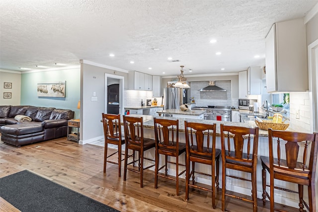 kitchen featuring light wood-style flooring, tasteful backsplash, wall chimney exhaust hood, white cabinets, and range