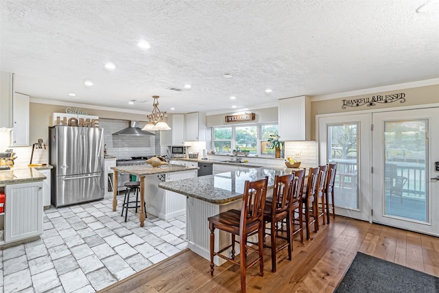 kitchen featuring light wood-type flooring, a kitchen island, stainless steel appliances, a breakfast bar area, and wall chimney range hood