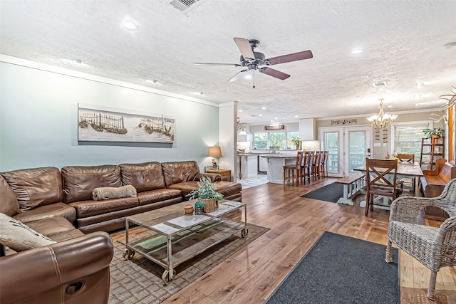 living room with hardwood / wood-style floors, crown molding, ceiling fan with notable chandelier, and a textured ceiling