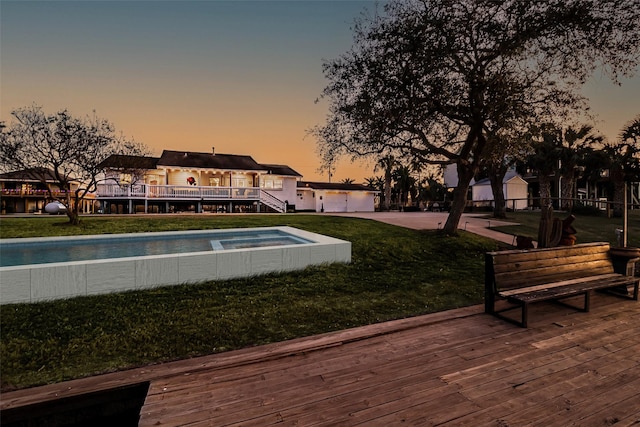 pool at dusk featuring an outdoor pool, a wooden deck, stairs, and a yard