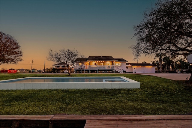 pool at dusk with a lawn, an outdoor pool, and a wooden deck