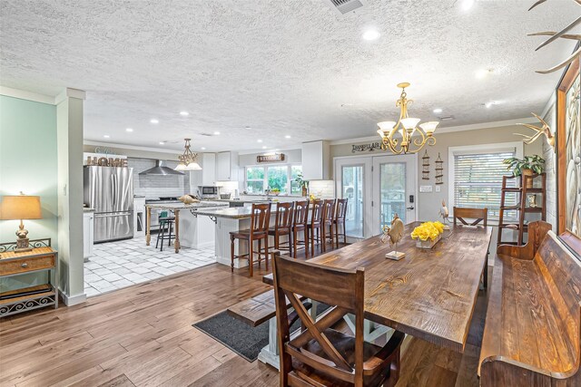 dining area featuring crown molding, light wood-style flooring, a notable chandelier, and a wealth of natural light