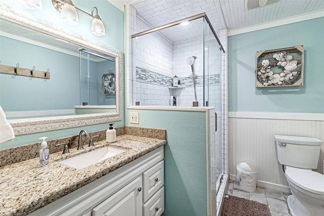 bathroom with a wainscoted wall, a stall shower, toilet, and vanity