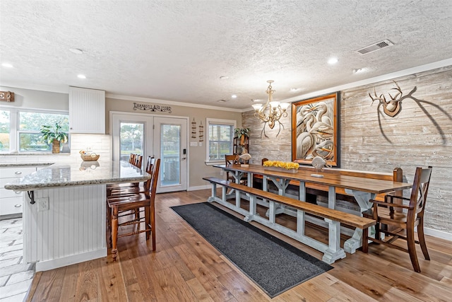 dining room featuring light wood finished floors, visible vents, ornamental molding, an inviting chandelier, and a textured ceiling