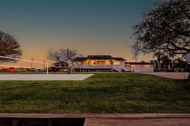 exterior space with concrete driveway, a garage, a lawn, and volleyball court