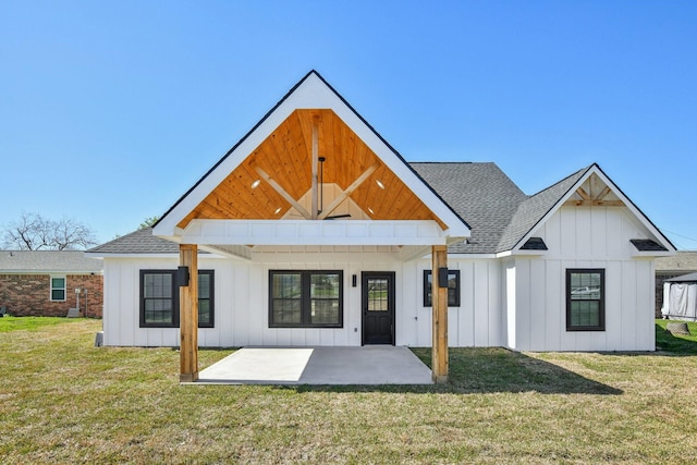rear view of property with a yard, board and batten siding, a shingled roof, and a patio