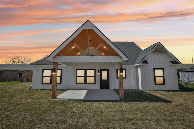 back of house at dusk featuring a patio, a yard, and board and batten siding