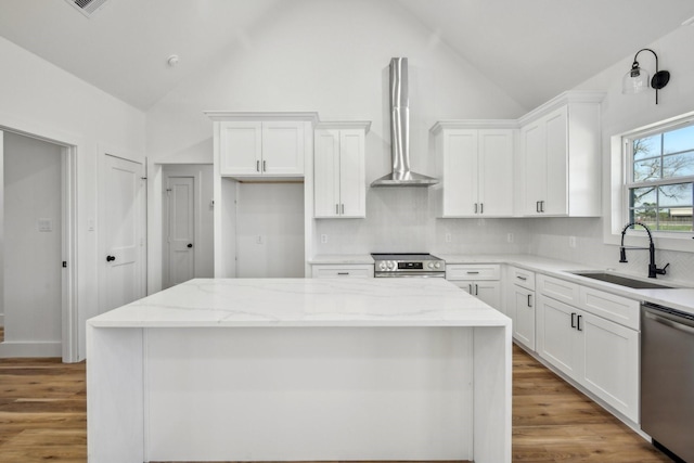 kitchen featuring light stone counters, white cabinets, stainless steel appliances, wall chimney exhaust hood, and a sink