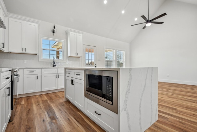 kitchen with white cabinetry, stainless steel range with electric cooktop, light wood finished floors, built in microwave, and ceiling fan