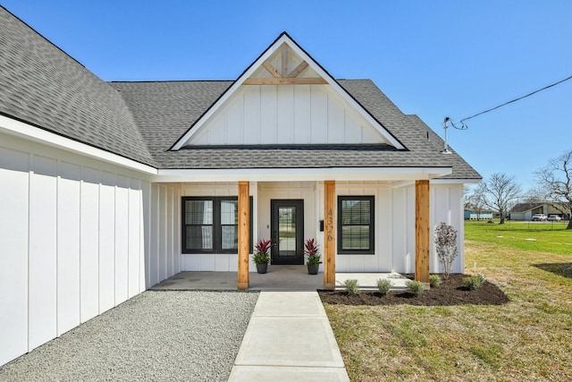 entrance to property with covered porch, board and batten siding, a shingled roof, and a lawn