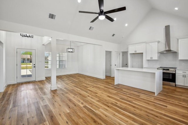 kitchen with visible vents, stainless steel range with electric stovetop, wall chimney range hood, open floor plan, and light countertops